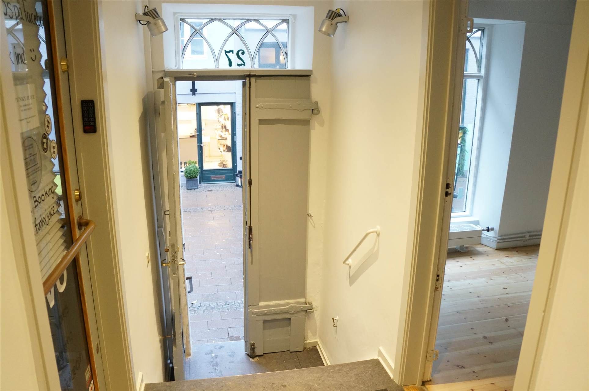 Opgang til et butikslokale i Fiolstræde med åben dør og udgang til en butik med vinduer og plante