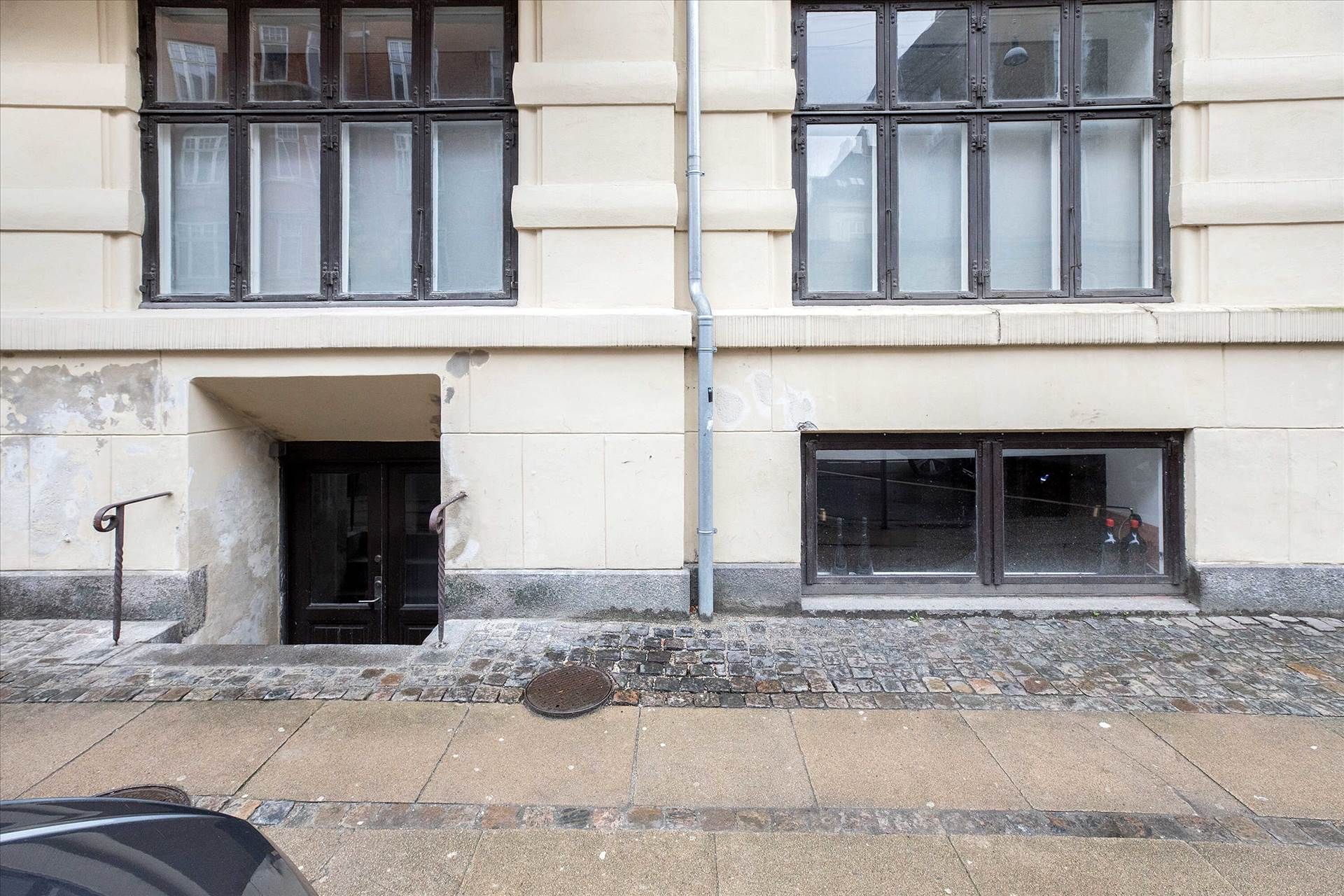 Et to-etagers lejlighedshus med en lyseblå røgslange og en halvmands høj bjælke. En mørk dør og et sølvfarvet stigehåndtag.