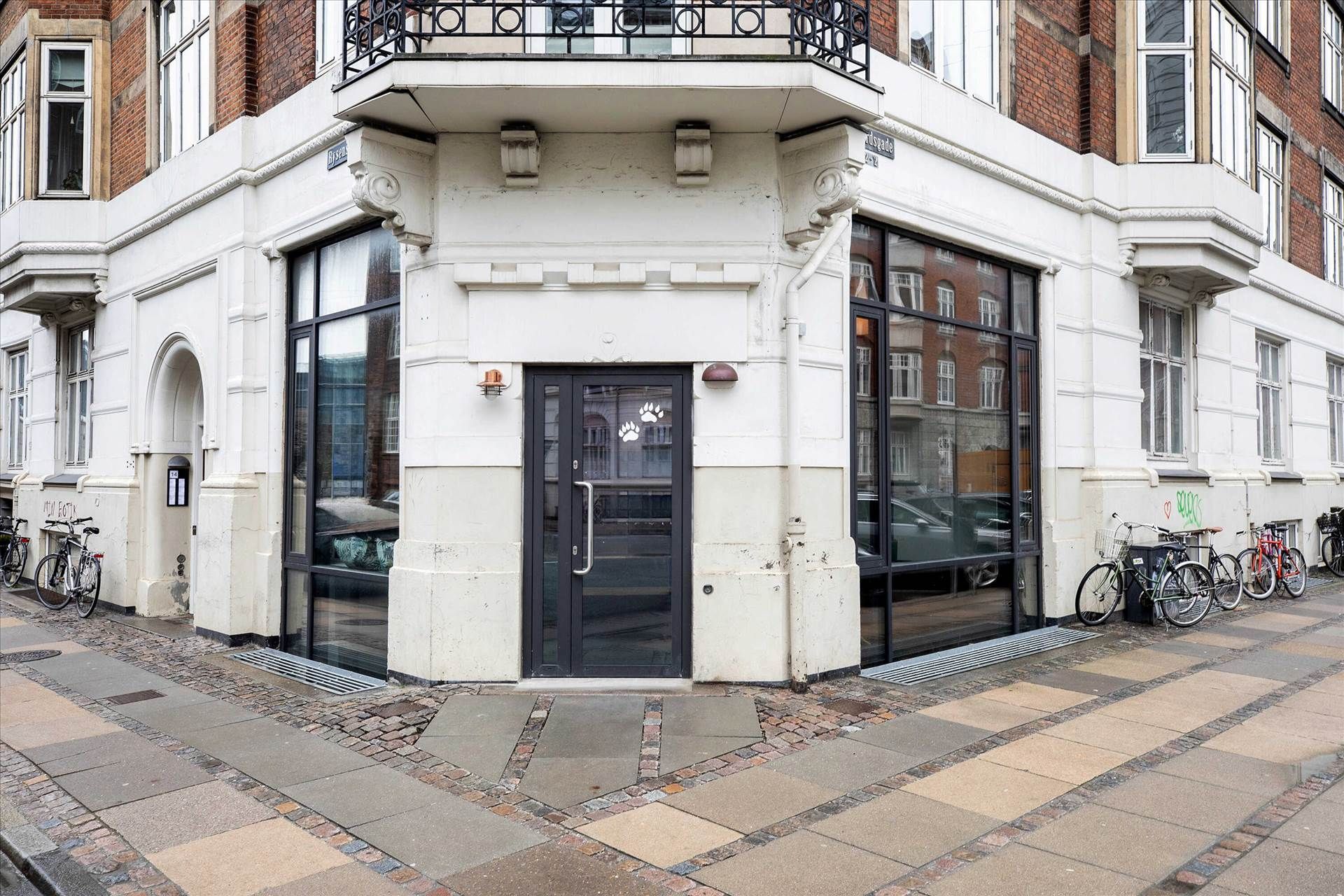 En gård med to høje huse med glasruder og et stort glasdøre med et motiv på døren. To cykler står parkeret på højre side af
