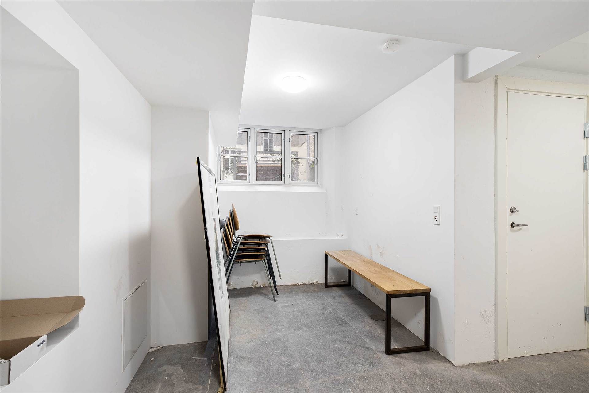 En tom og nyrenoveret lejlighed med hvide vægge, et vindue og en lille åbning med en brædderkasse mod væggen