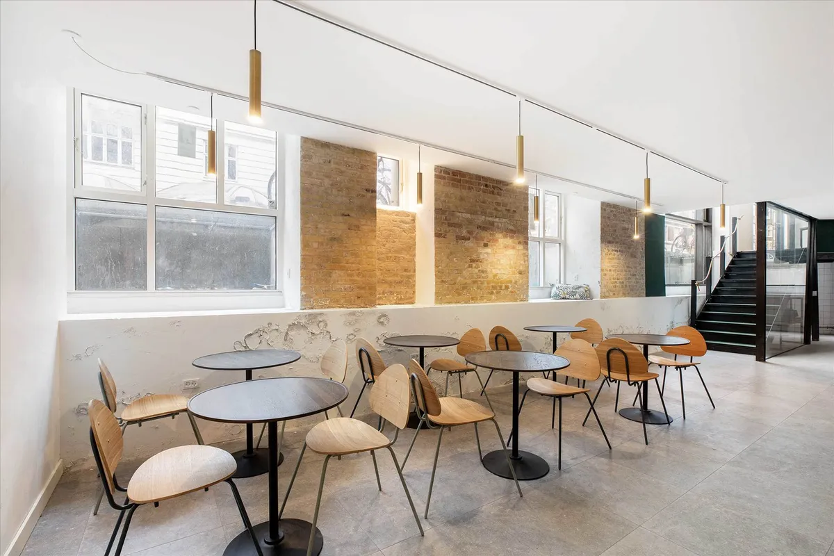 Møbelserie med rundt bord og stol i en café med møbler og vinduer i baggrunden