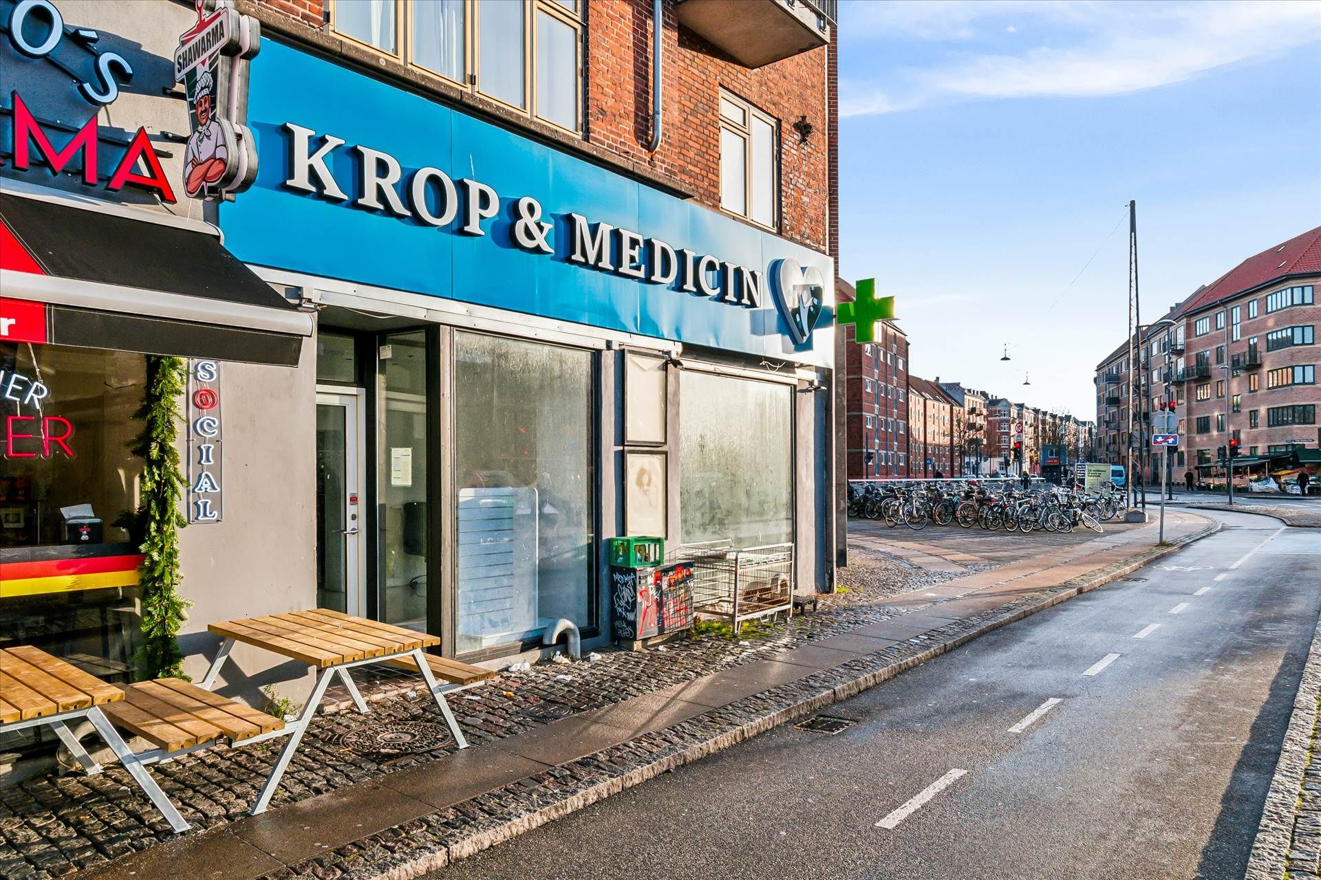Butik med navnet Krop & Medicin og en skovl med navnet Shawarma er placeret i et bykvarter. Der er flere cykler parkeret ved