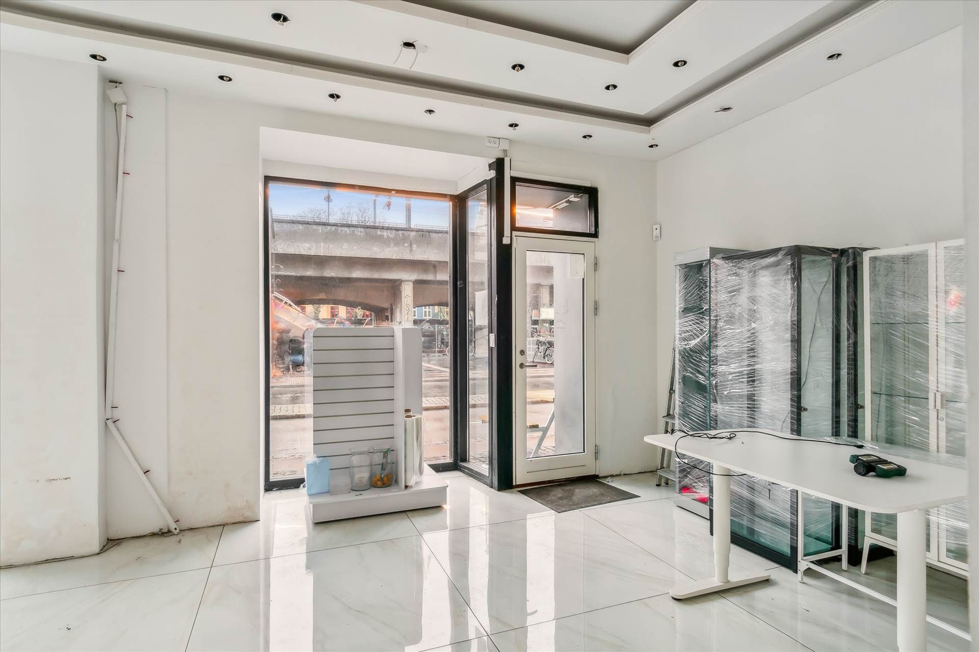 Et tomt og nyt lokale med hvidt loft og gulv samt store vinduer og døre til gaden og udenfor.