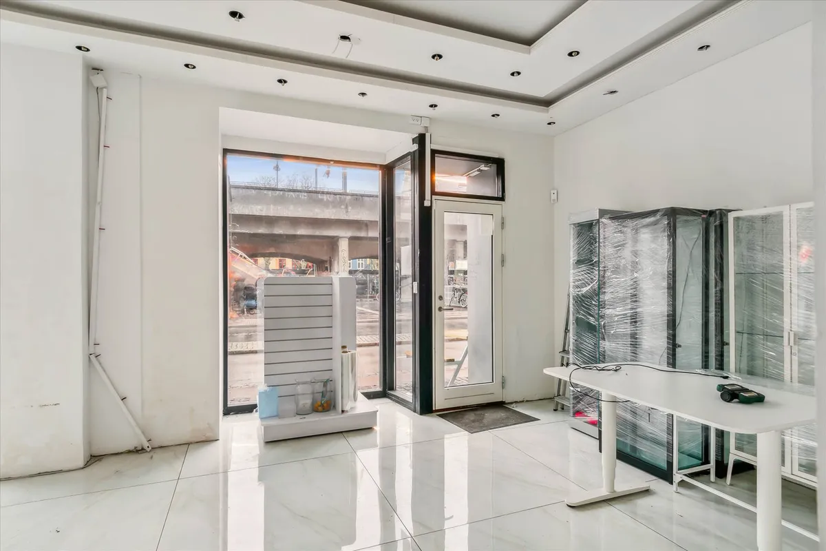 Et tomt og nyt lokale med hvidt loft og gulv samt store vinduer og døre til gaden og udenfor.