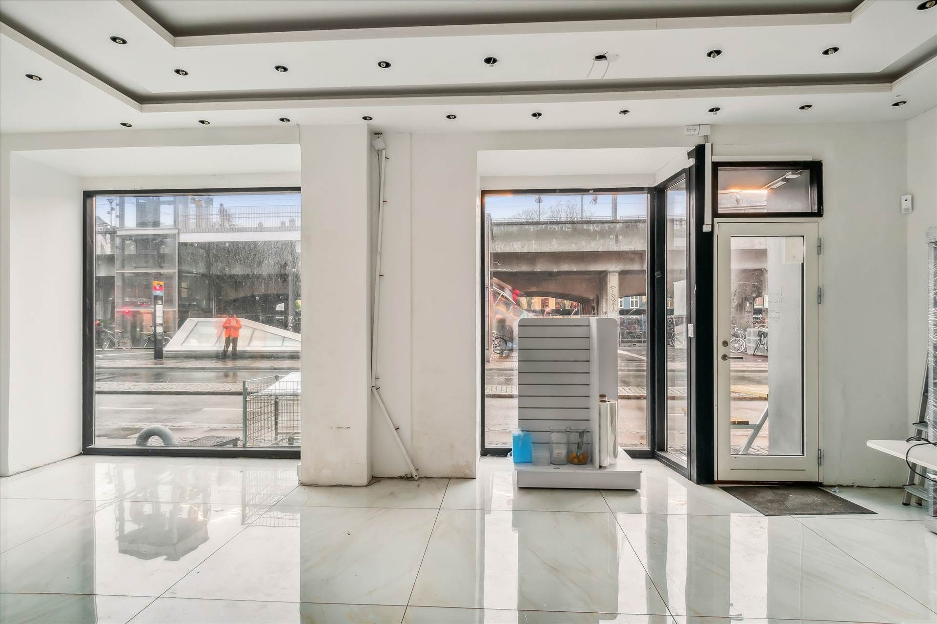 Store hvide lofter og vægge samt hvide gulvfliser. Glasdøre og vinduer samt lager og møbler i butikken