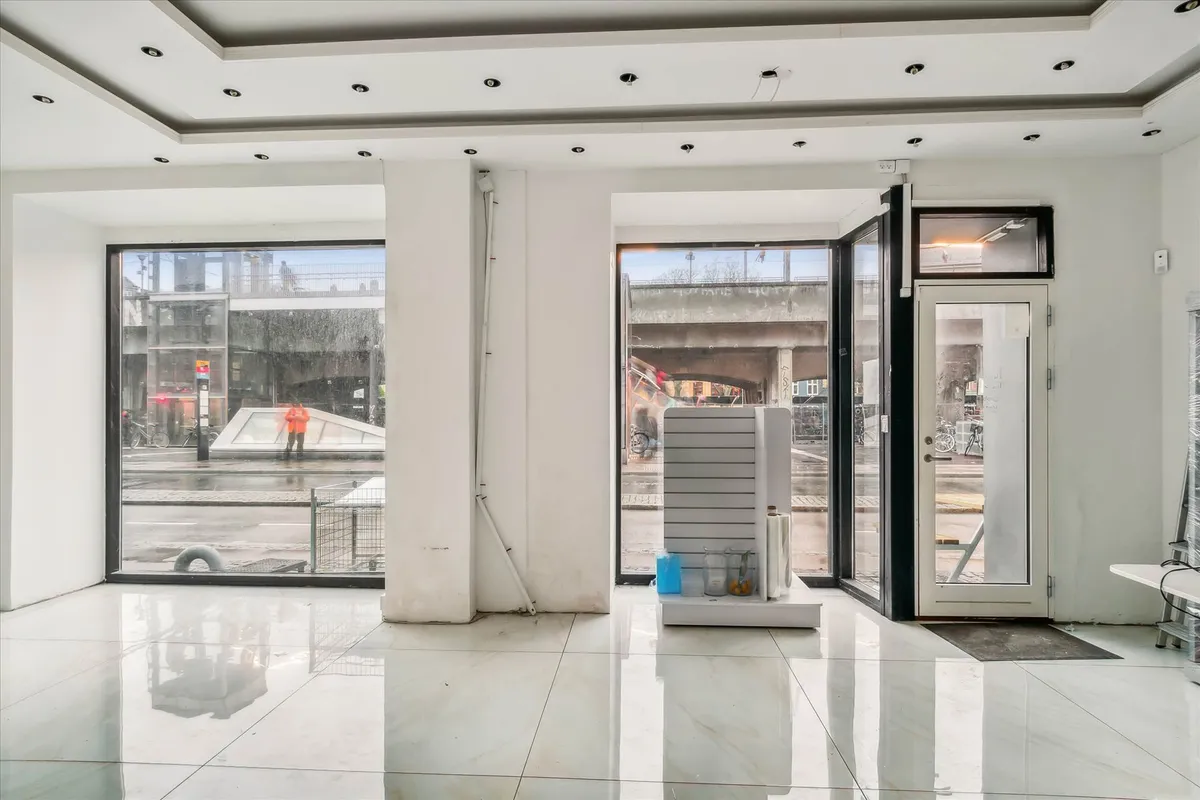 Store hvide lofter og vægge samt hvide gulvfliser. Glasdøre og vinduer samt lager og møbler i butikken