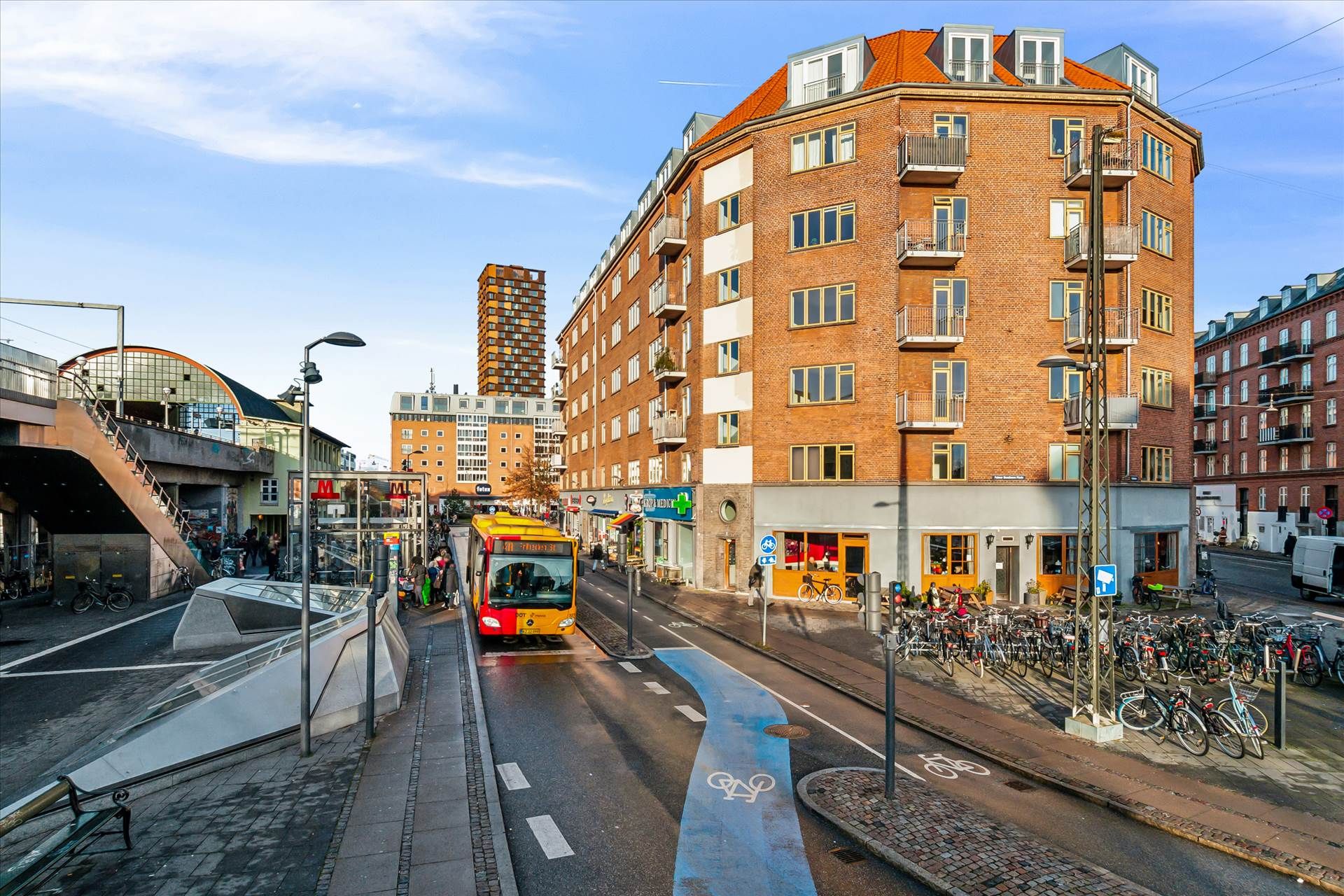 Butiksbygning med røde mursten og højdeskille mellem gader og cykelstier på Nørrebro i København. Biler og busser kører på