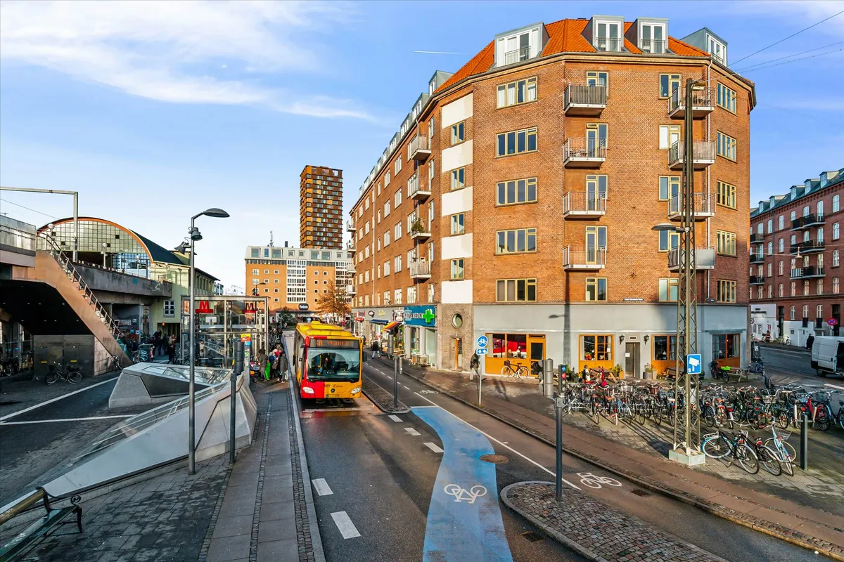 Butiksbygning med røde mursten og højdeskille mellem gader og cykelstier på Nørrebro i København. Biler og busser kører på