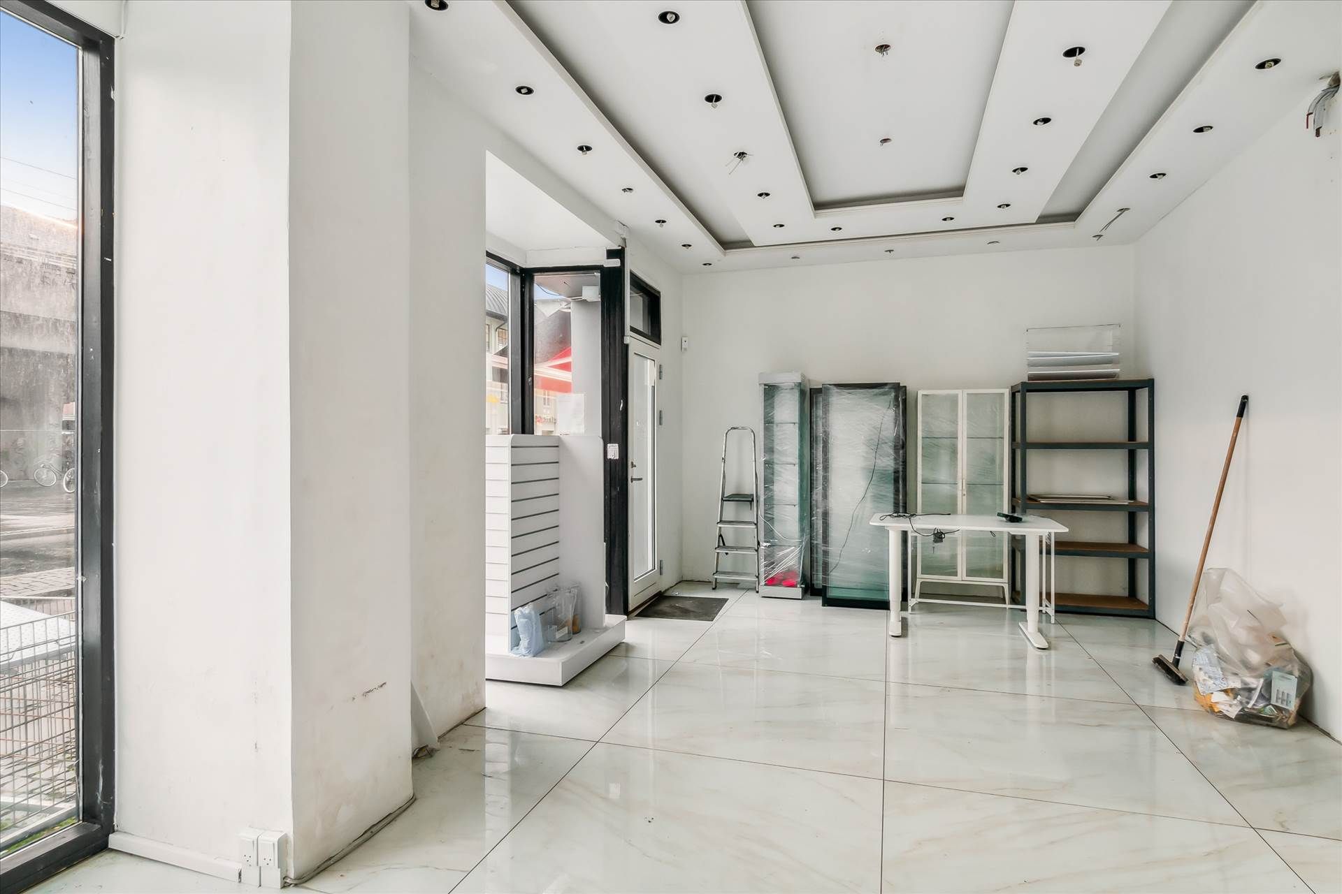 Indenfor en ren, lyskaret butikslokal, udstyr med marmorgulve og hvide vægge. Der er en åben dør og vinduer samt flere