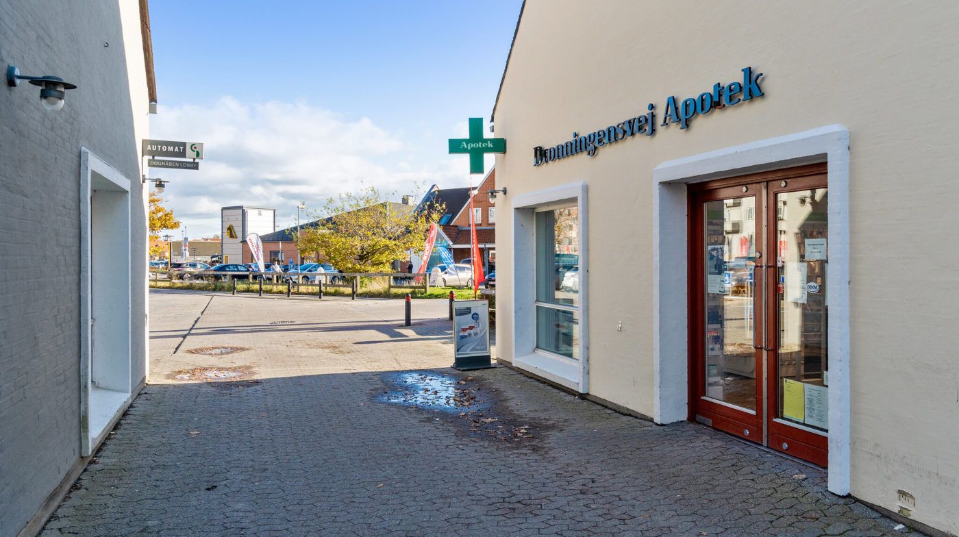 En afgangsvej fører til et rødt dørpar med navnet Dønningensvej Apotek, samt en grøn Apotek-skilt på facaden