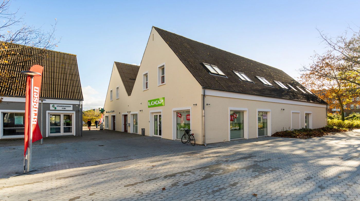 Store bygninger med røde flag og knaplader foran. En cykel står foran det ene vindue. En person går bagved på gaden.