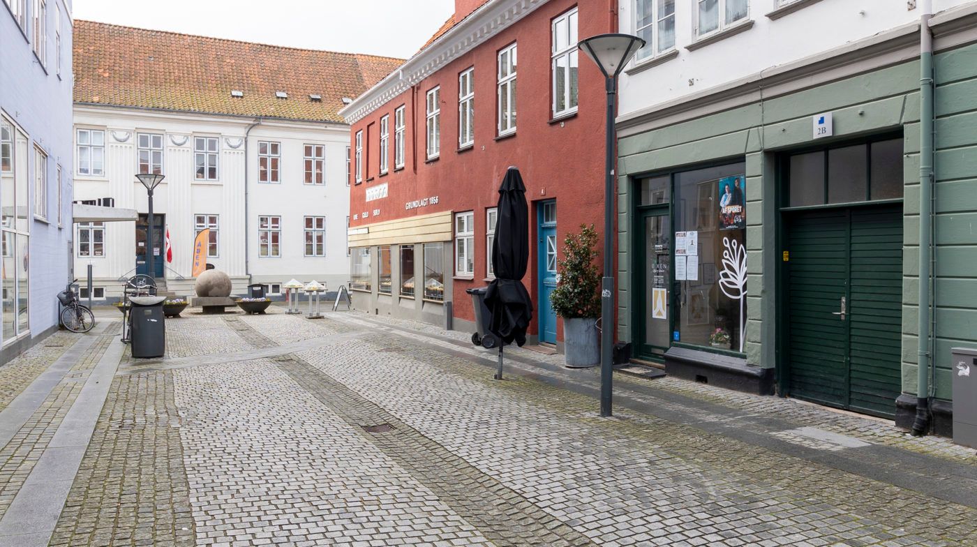 Forladt stenbrolægget gade i Nyborg med butikker, en lukket paraply og en lukket butiksdør med nummer 2B
