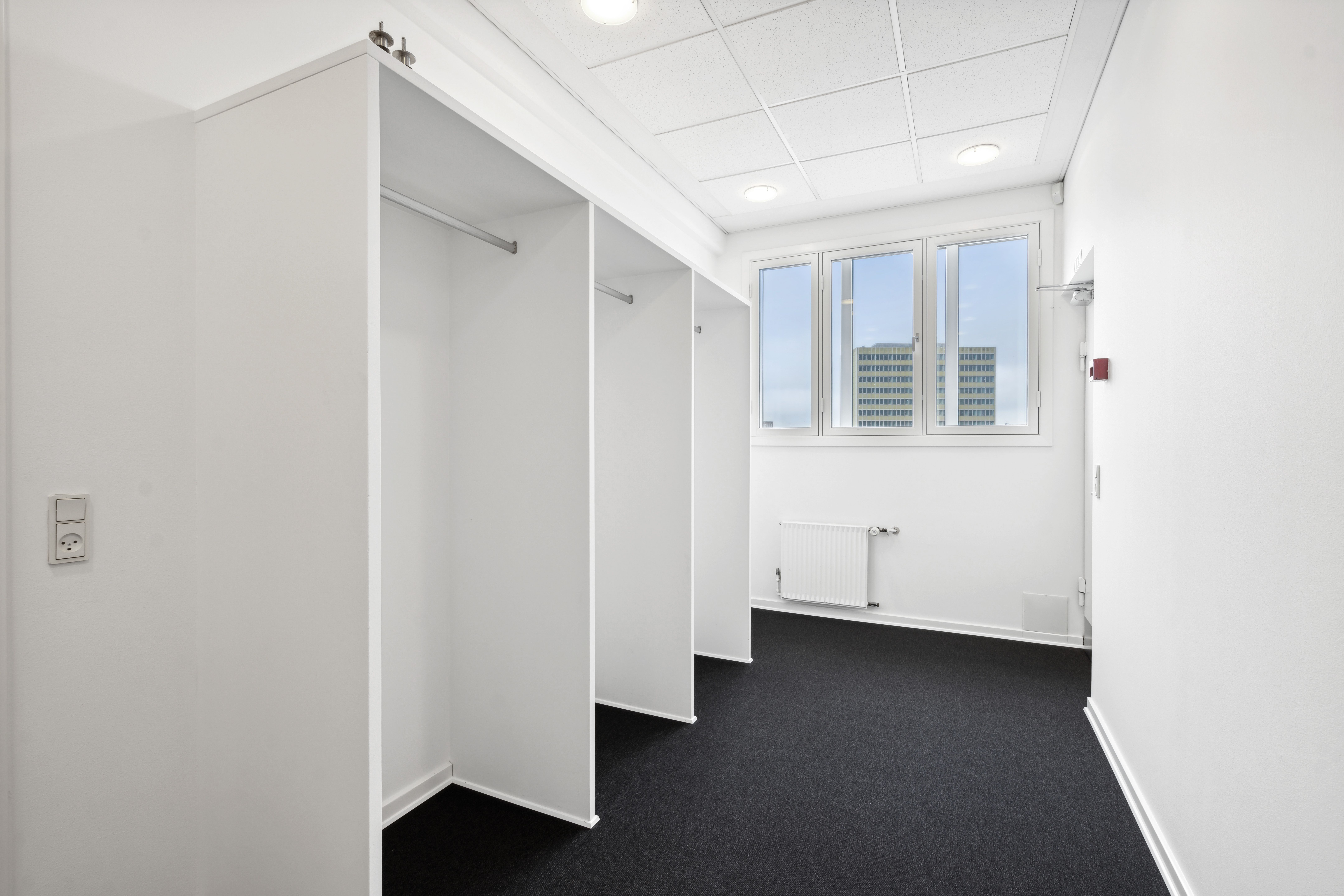 Lukket garderobeskab med en hvid væg og gulv og et vindue med udsigt til et højhus i baggrunden