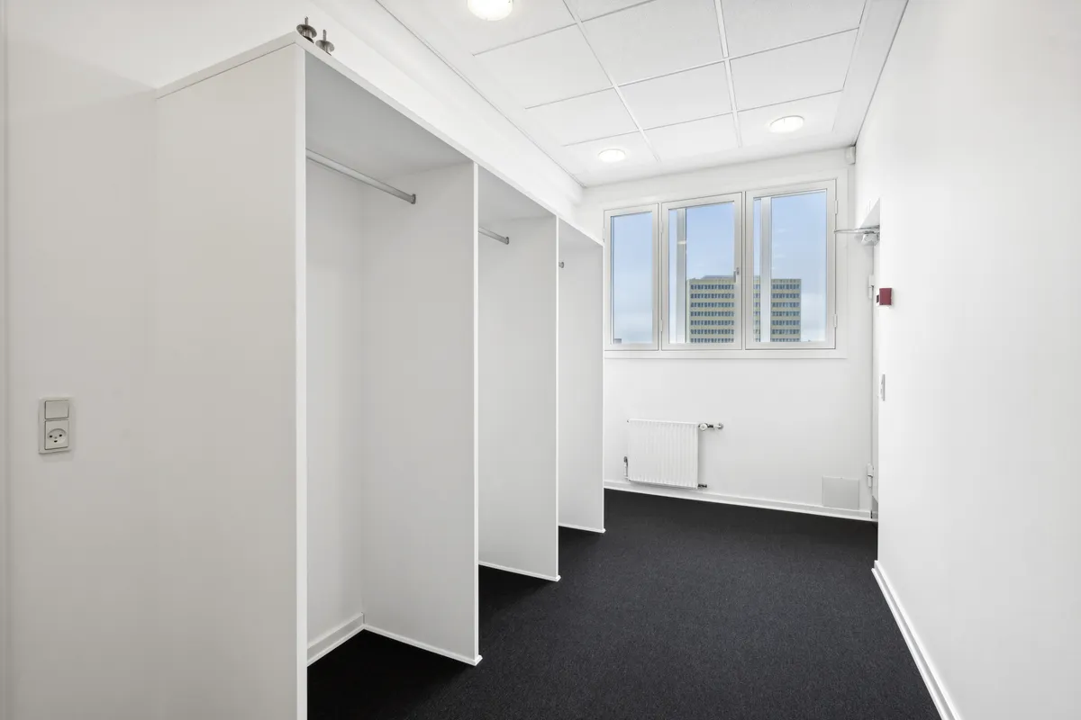 Lukket garderobeskab med en hvid væg og gulv og et vindue med udsigt til et højhus i baggrunden
