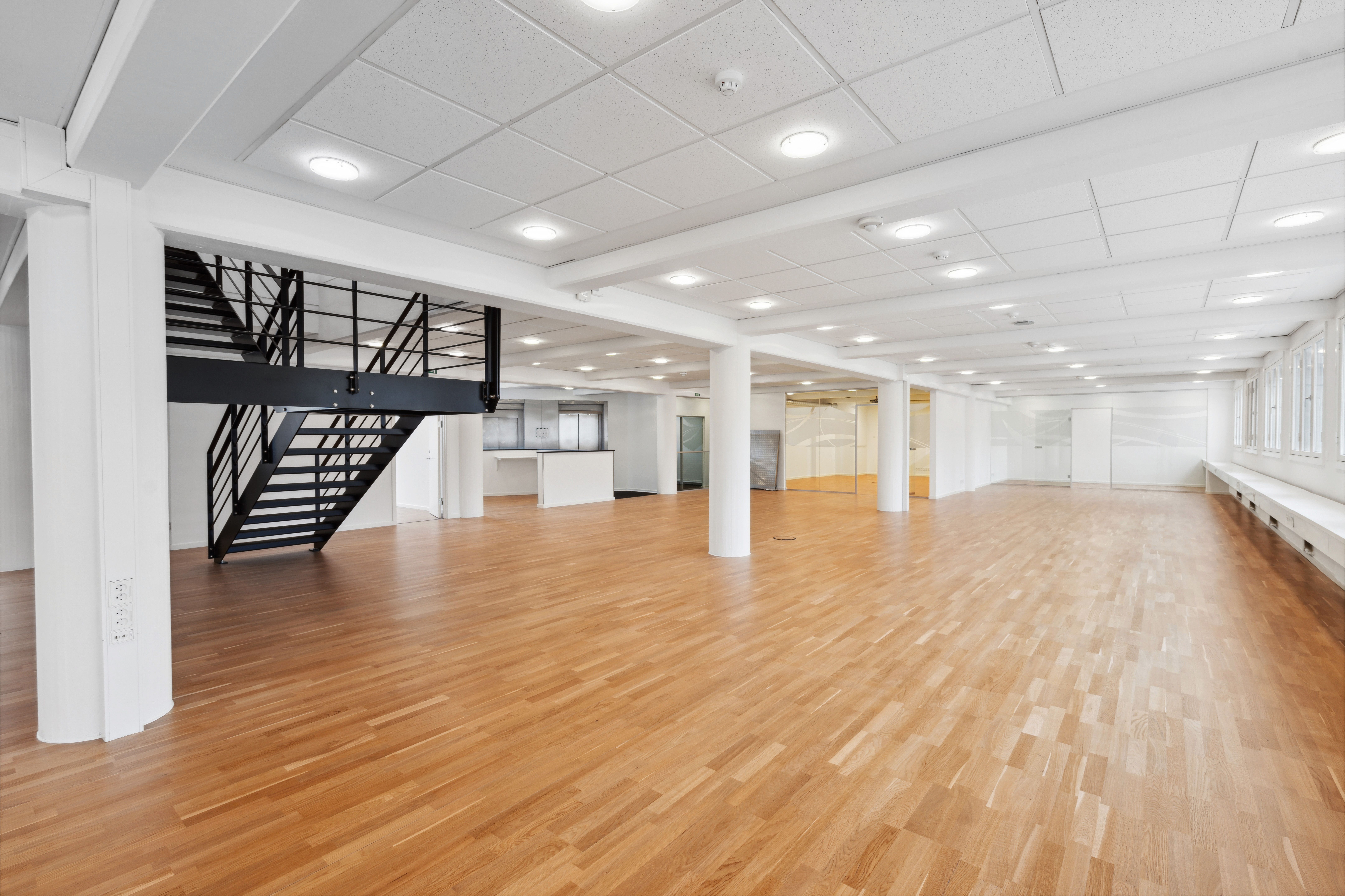 Inde i et lejemål med lyse gulve, lyse lofter, lyse vægge og et stort vindue i enden af rummet, der vender ud mod en gårdhave