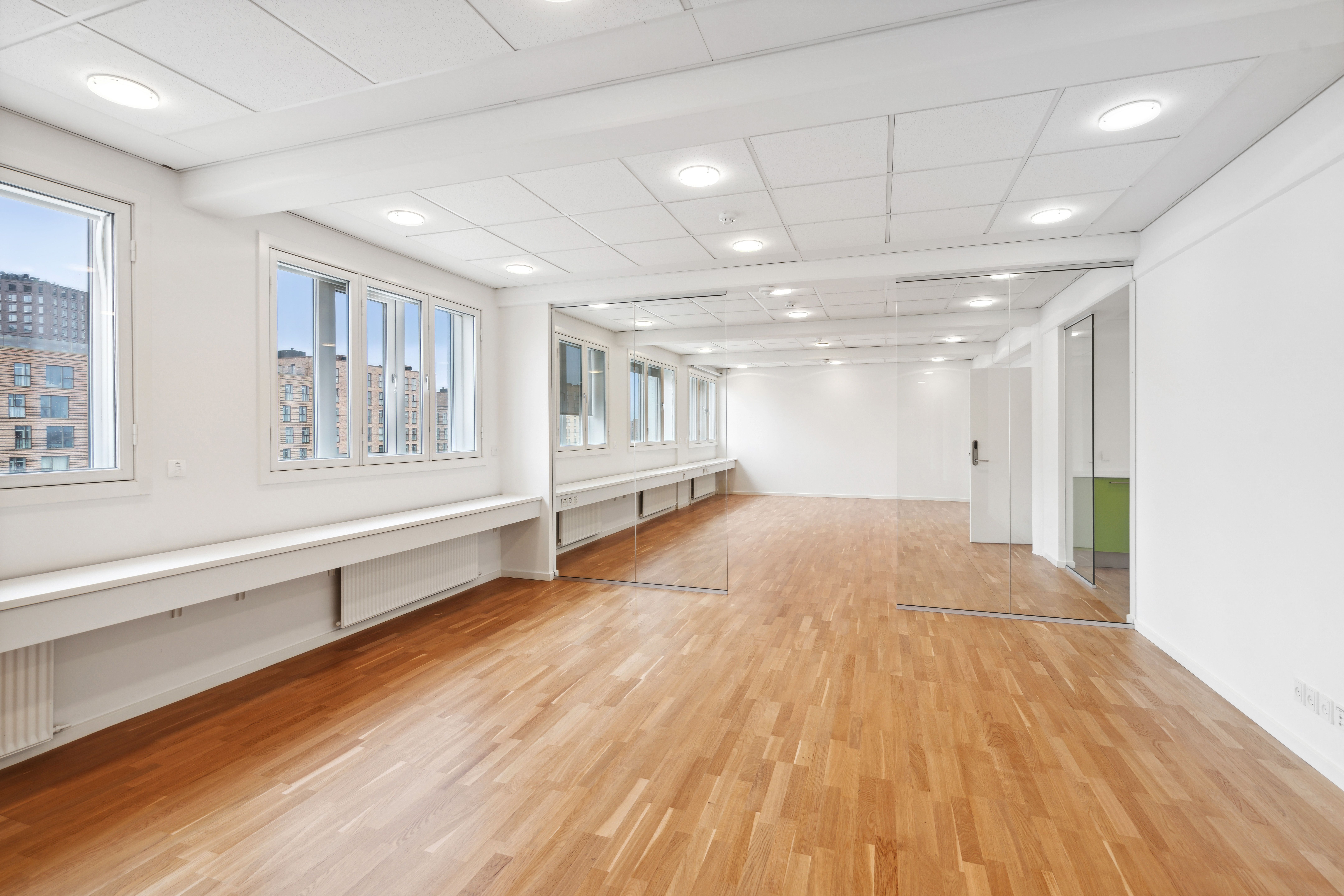 Rummeligt lejemål med højloft, lyse vinduer og spejlede vægge og døre. Forhøjede hvide sokkel og hvide vægge samt trægulv