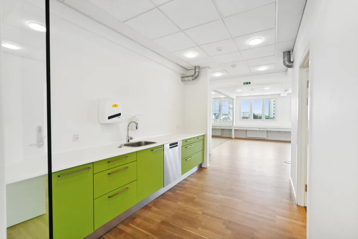 Rent og moderne køkken med lyse grønne skabe, hvidt arbejdsbord og en rustfri stål ovn placeret ved siden af en vandhaner