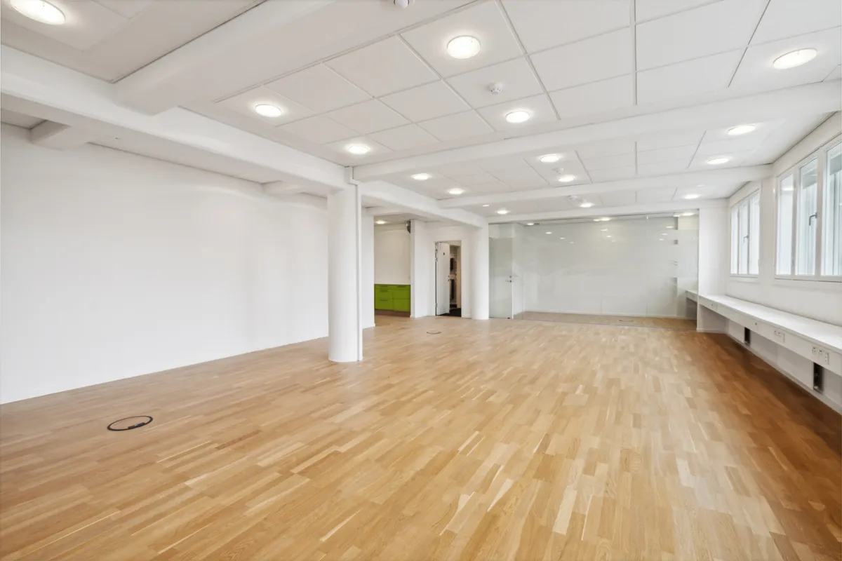 Moderne kontorrum med højloft og lysegule loftspaneler samt trægulve og lysegrå vægge og vinduer