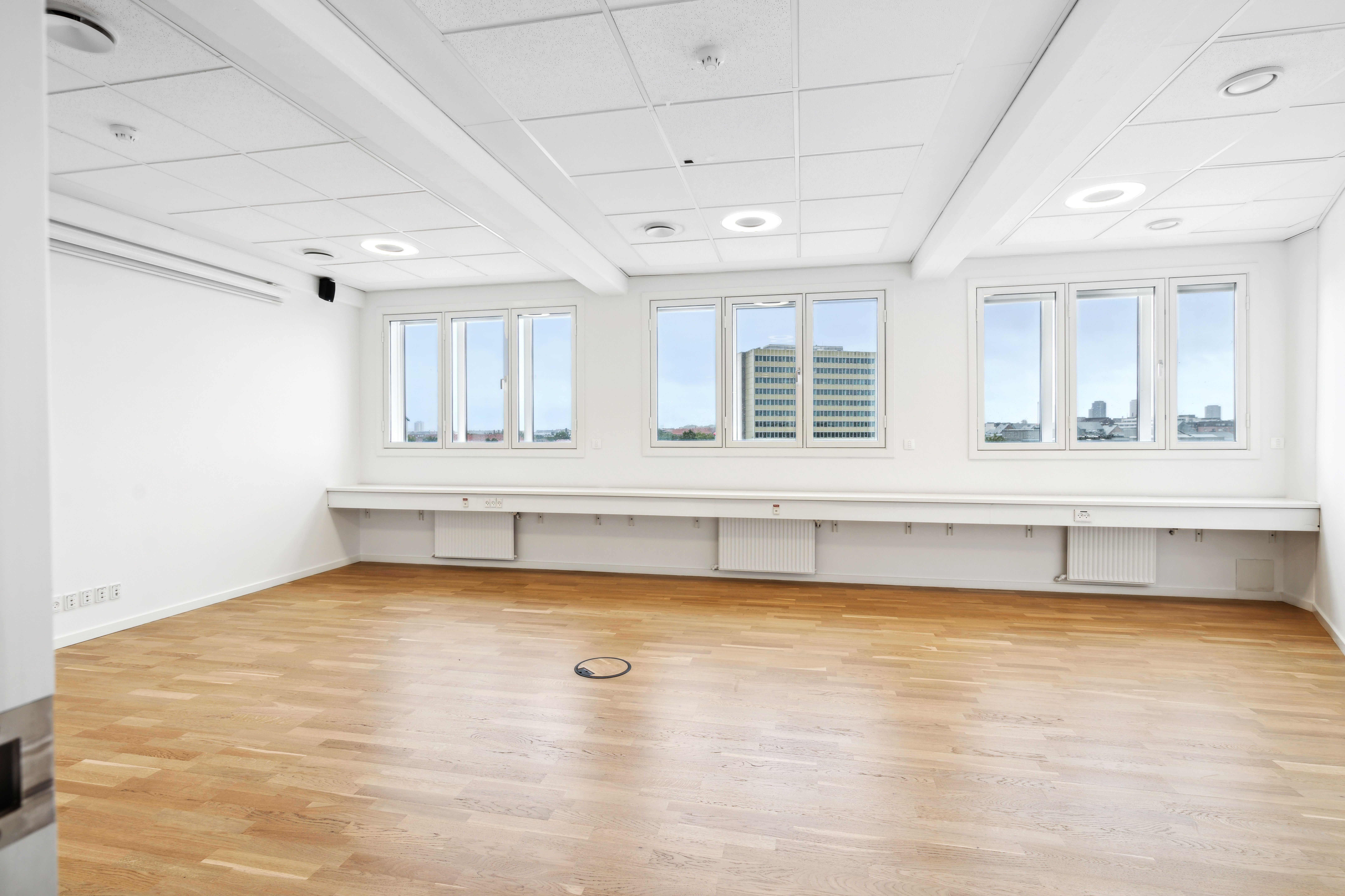 Lejemål med moderne hvide vægge, lyse gulve og vinduer med udsigt til bygninger og bylandskab Værelset er fuldt møbleret med