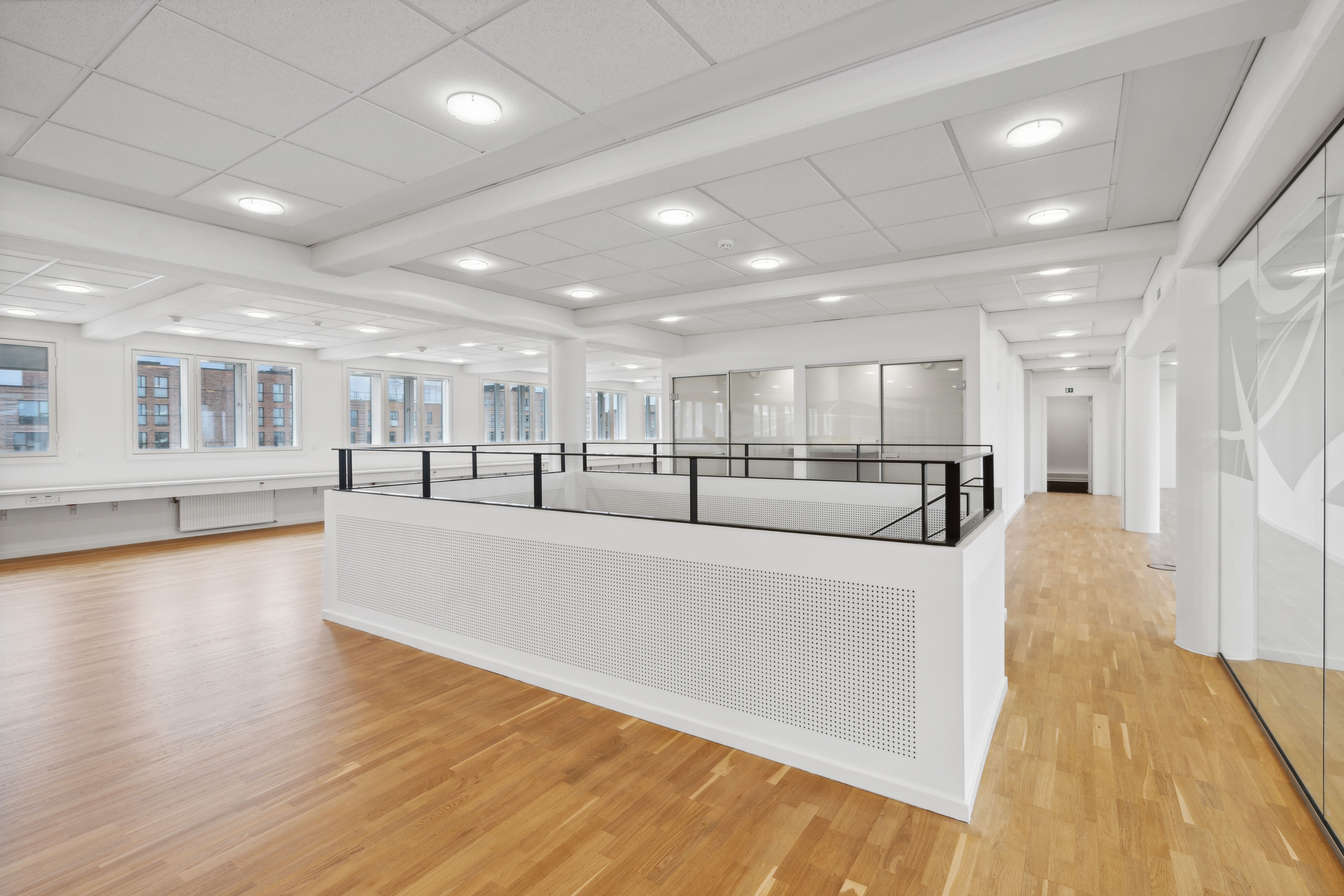 Rummeligt kontor med højloft, hvidt gulv og glas. Moderne loftskonstruktion med indlejrede pære. Mellemgulve med hvid væg og