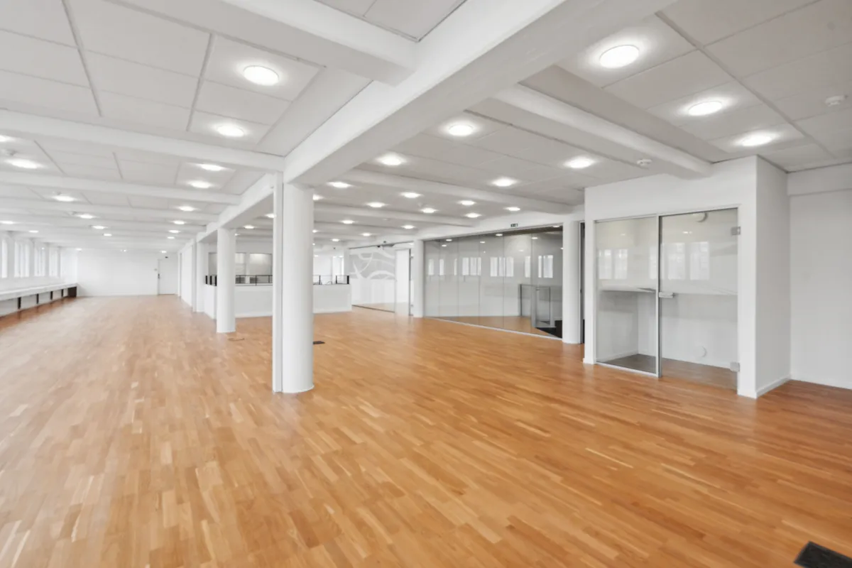 Rummeligt kontor med lyse trægulve og hvide vægge. Styrende loftsbjælker og glasvinduer for eksempel.