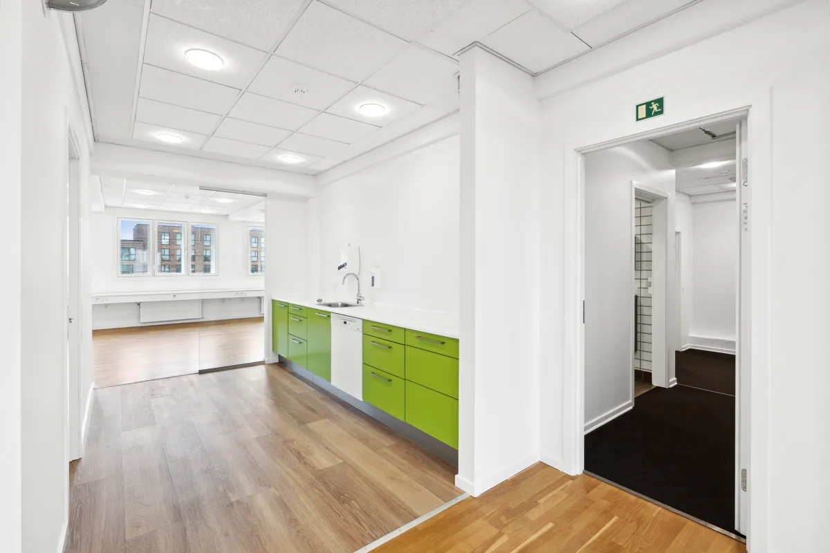 Rummelige lokaler med hvide vægge og grønne skabe. Værelset har en hvid vaskemaskine og en lysegrå gulvbelægning. Der er et