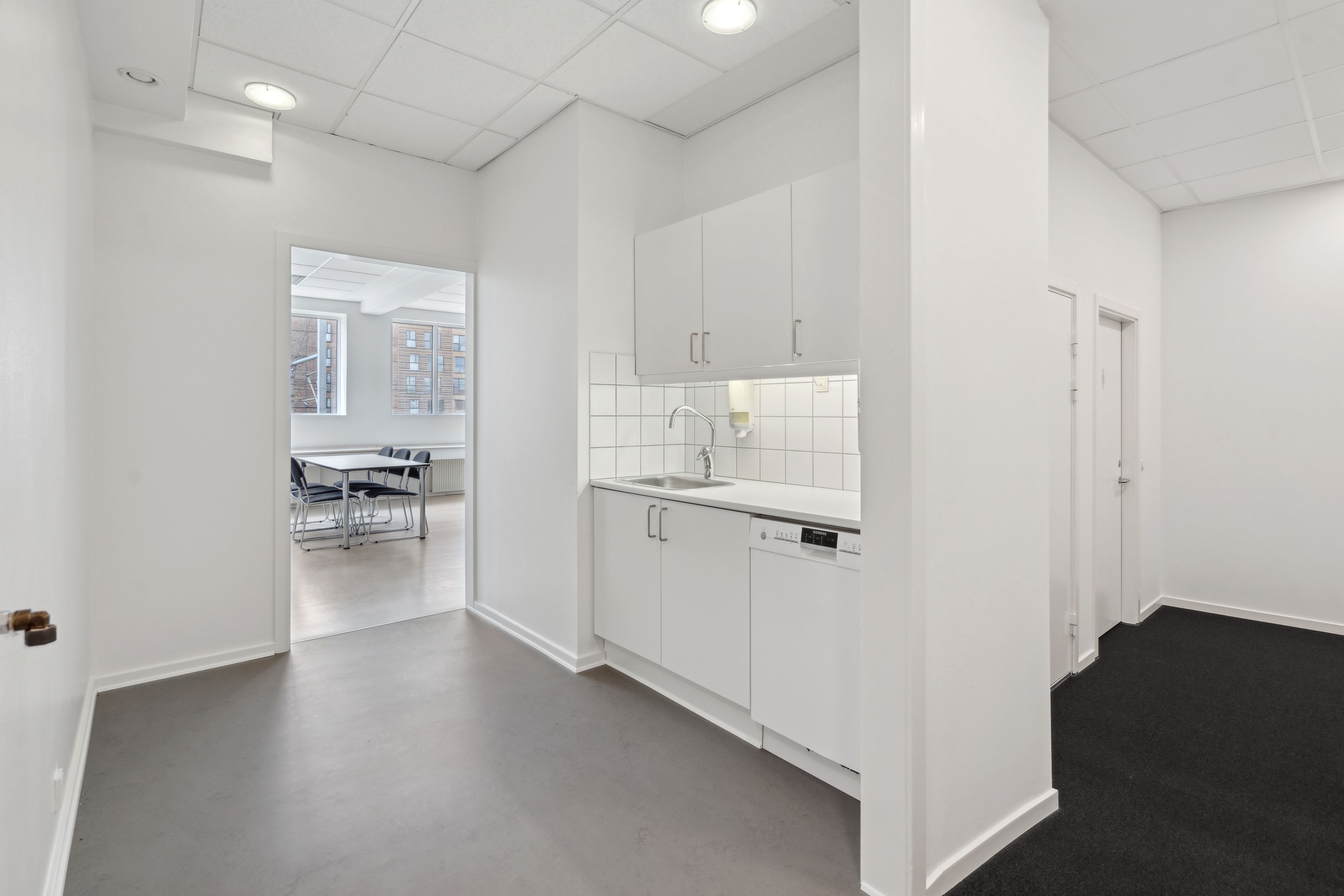 Et rent køkken med hvidt loft og hvide vægge. Der er et vaskebækken med vandhane og et spidset køleskab. Der er et