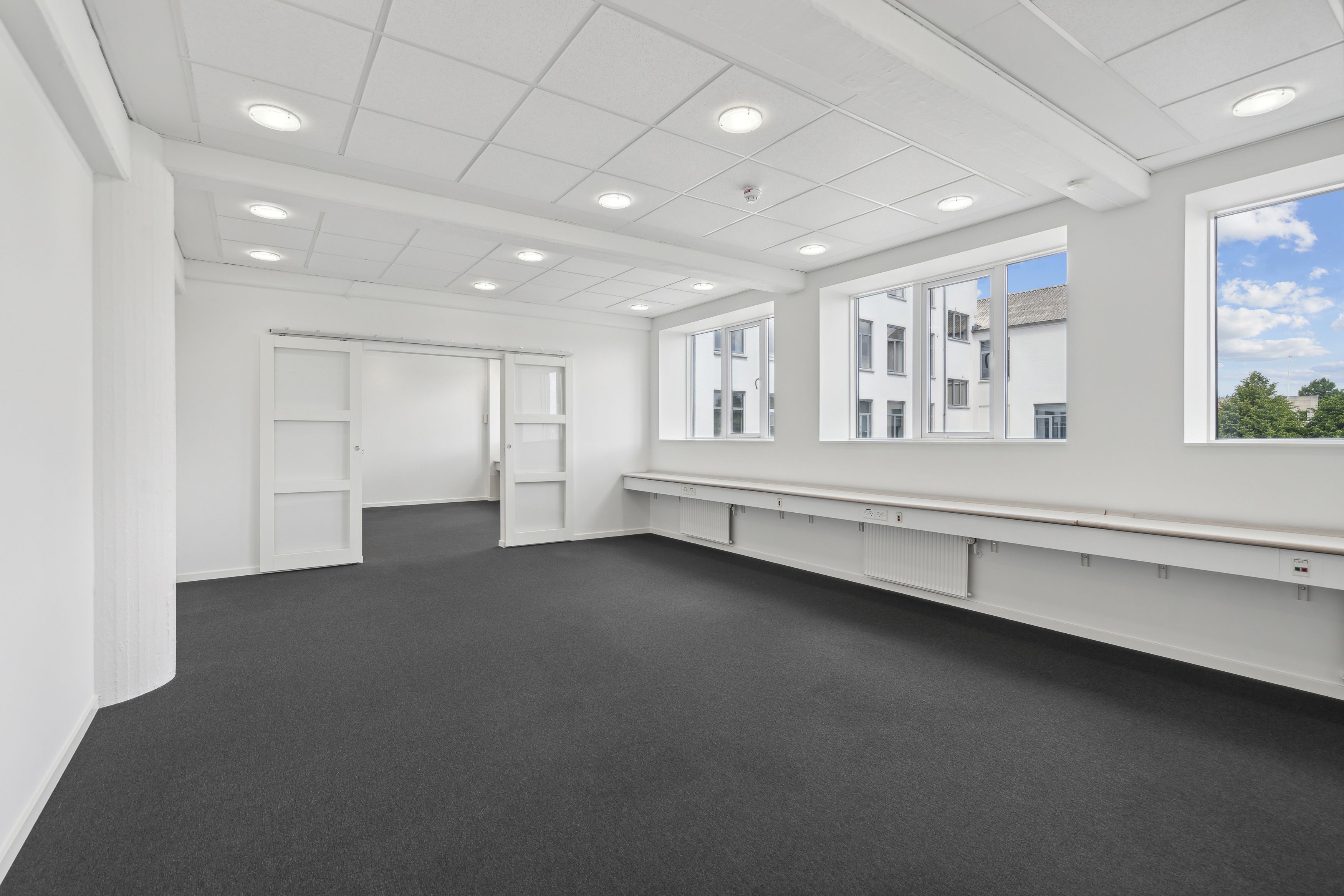 Lejlighed med lyse loftsrum og store vinduer i et moderne hvidt rum med gulvbelægning og åbne døre