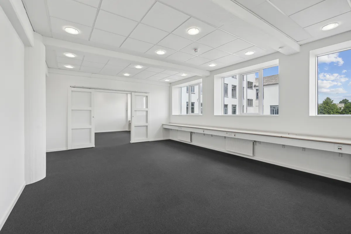 Lejlighed med lyse loftsrum og store vinduer i et moderne hvidt rum med gulvbelægning og åbne døre