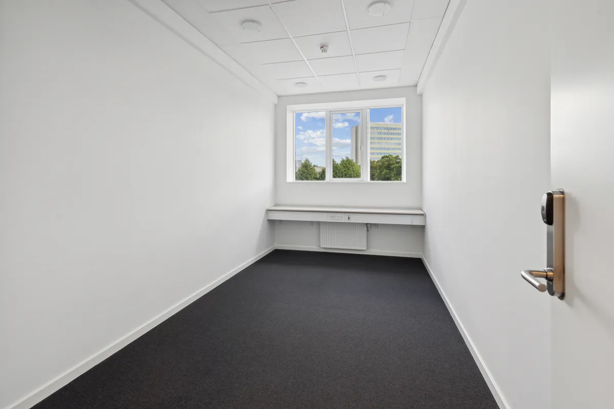 Moderne, tomt kontor med hvide vægge, gulv, loft, slanke radiator og et vindue med udsigt til bygninger og grønne træer