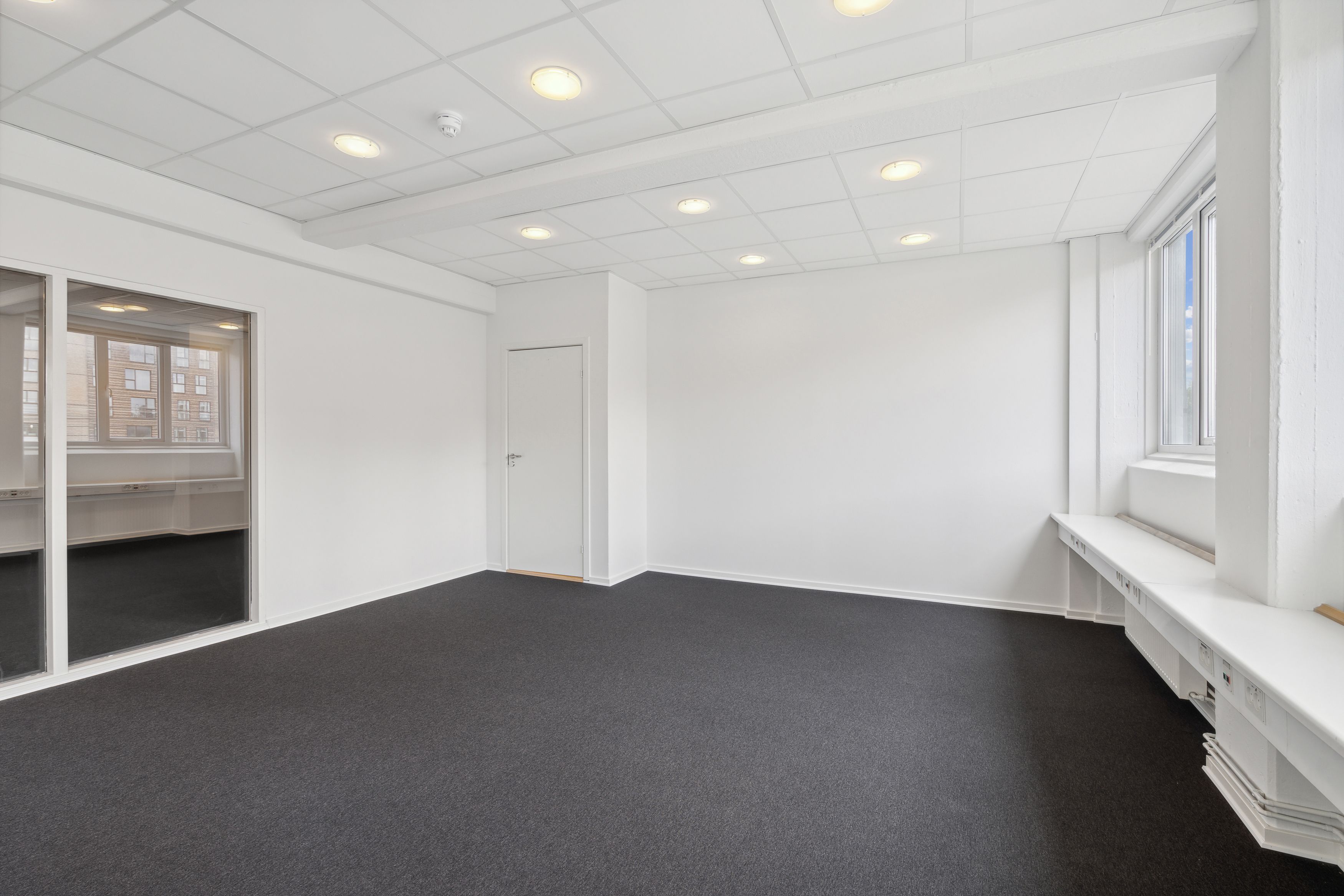 Lejemålet i Valby med hvide vægge og mørke gulve, glasdøre og vinduer med sollys, hvide lofter med indlejrede runde