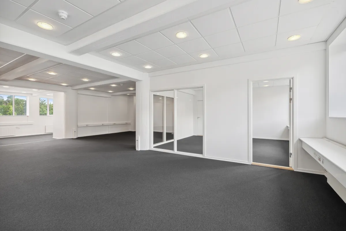 Værelse med glasdøre og hvide vægge, gulvbelægning og flere indbyggede lyspunkter på loftet, der er et vindue med udsigt til