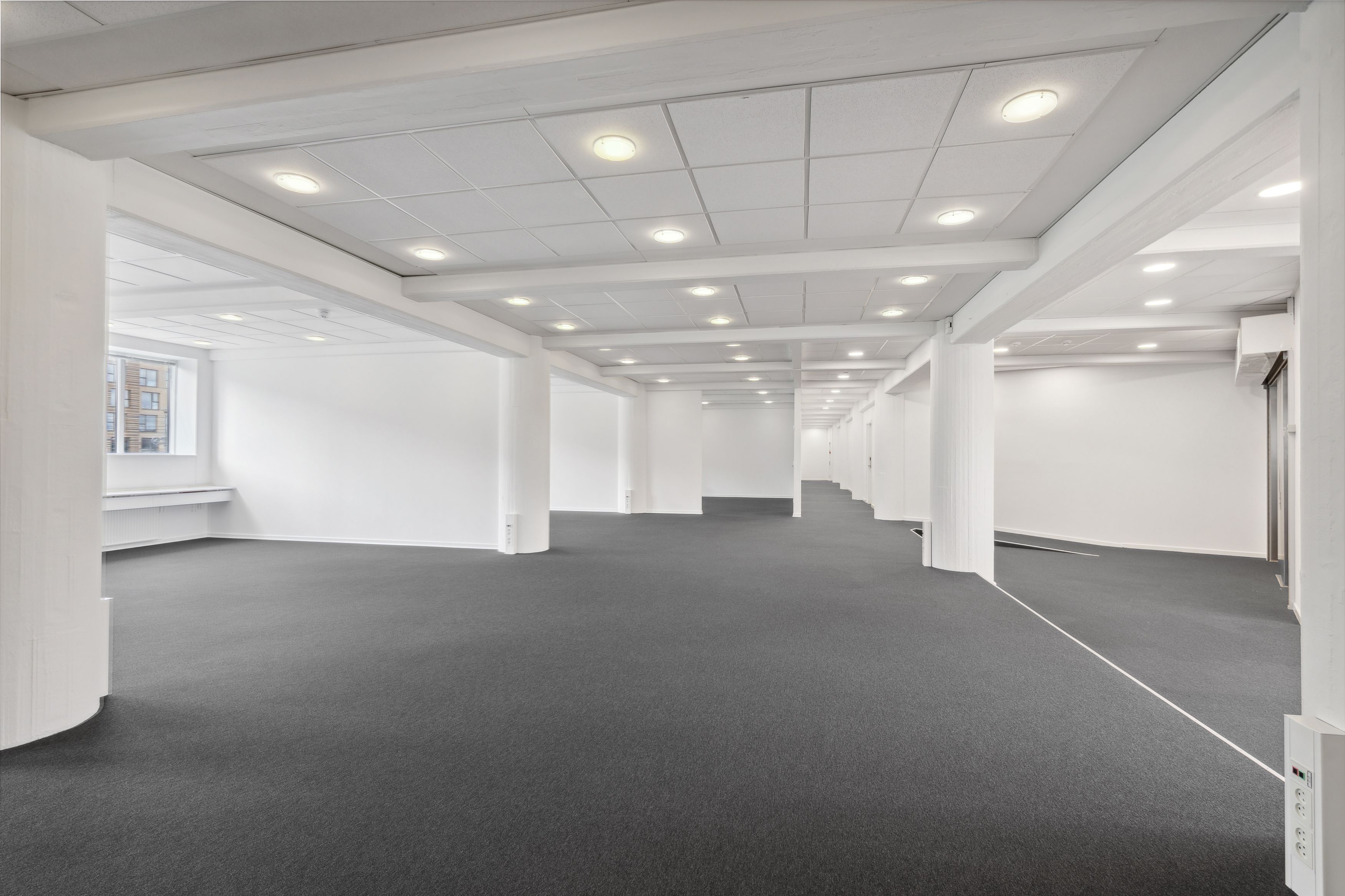 En stor, mørk gulvbelægning med flere hvide søjler og indbyggede lyspærer i loftet for at give god belysning.