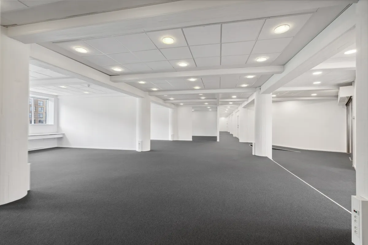 En stor, mørk gulvbelægning med flere hvide søjler og indbyggede lyspærer i loftet for at give god belysning.