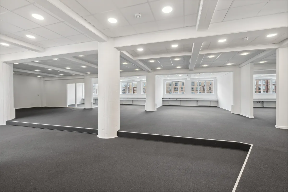 Store lokaler med højloft og lysegule loftslamper samt lysegrå gulvbelægning og hvide vægge. Højloftet krydses af hvide