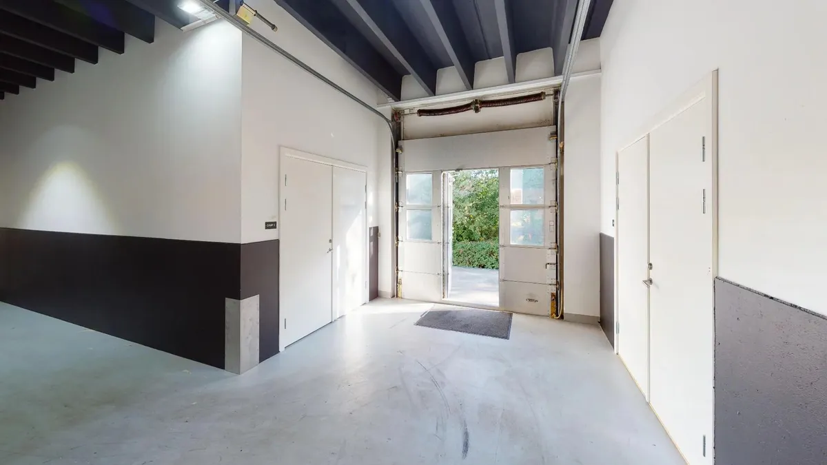 En lagerhal med hvide vægge og gulv samt højt loft med bjælker og to åbne døre og et glasvindue
