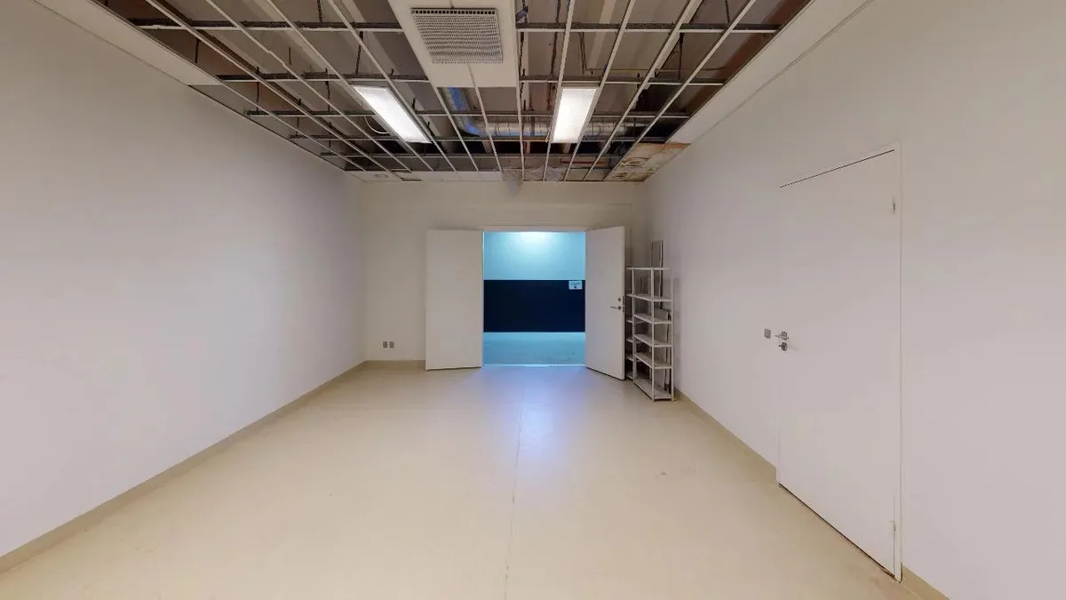 Store hvidmalede vægge med lyse gulve og metalliske lofter med indbygget lys. En hvid dør står åben, og et lager er synligt