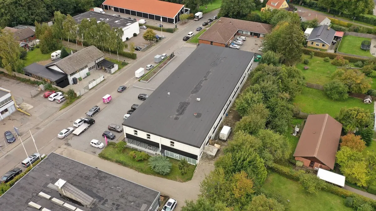 Forskellige bygninger med parkeringspladser og biler parkeret foran og bagved dem samt grønne græsarealer og træer