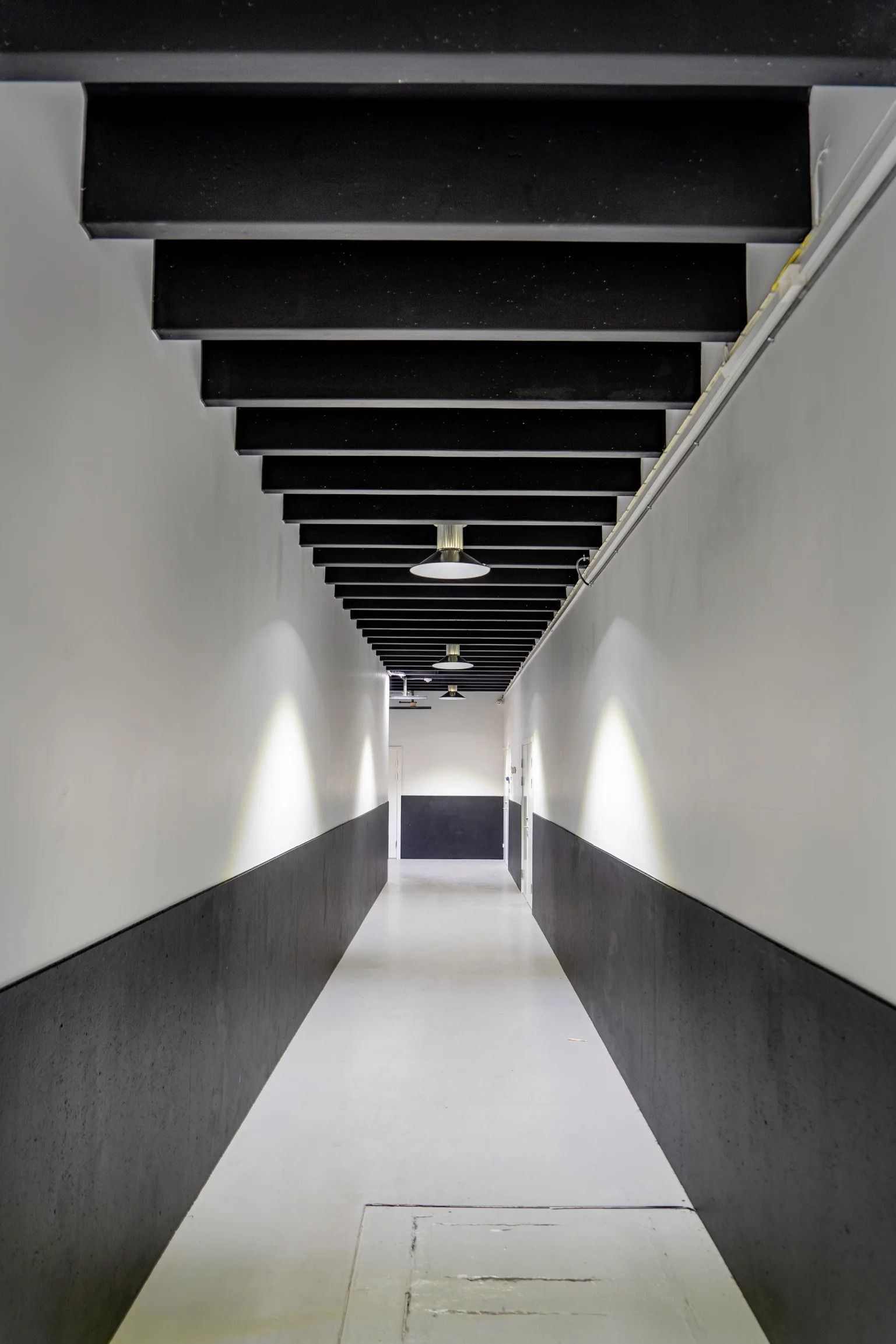 En længdevisning af en lysegang med hvide og sorte vægge, hvor der er et slankt loft med svage lamper