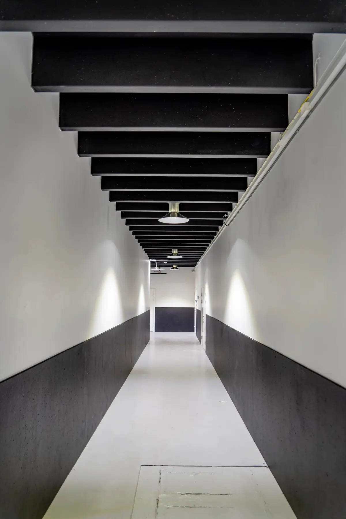 En længdevisning af en lysegang med hvide og sorte vægge, hvor der er et slankt loft med svage lamper