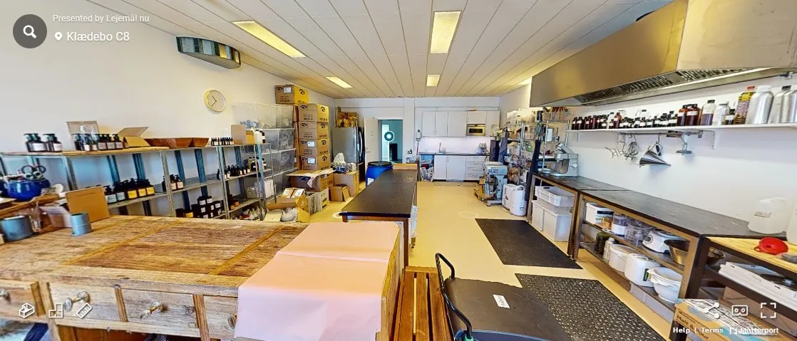 Lagerrum med træborde, køkkeninventar, flasker og bokse samt et hvidt køkken med mikrobølgeovn og vaskemaskine