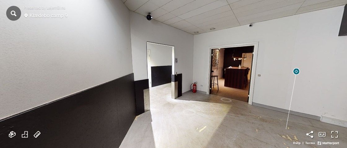 Indgangsområde med hvide vægge, sort og hvide vægfarver, døre og gulve, samt en brandslukker og sikkerhedskamera