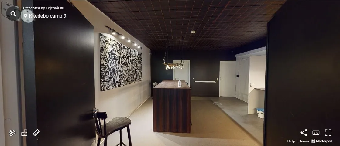 Sort og hvid kunstværk, lysekroner, køkkenbord og en stol i et lokale med hvide vægge og sort loft