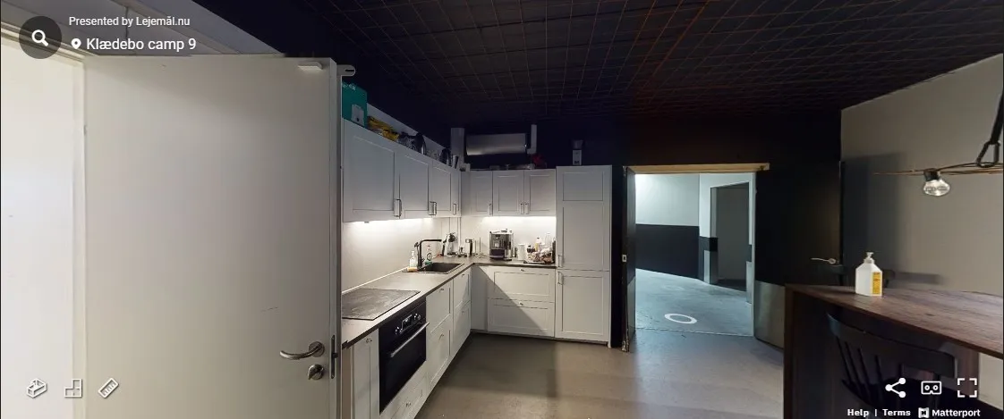 Et stort køkken med hvide vægge og loft samt hvide skabsfronter med lyse skarpe linjer og en stor køleskab i stående