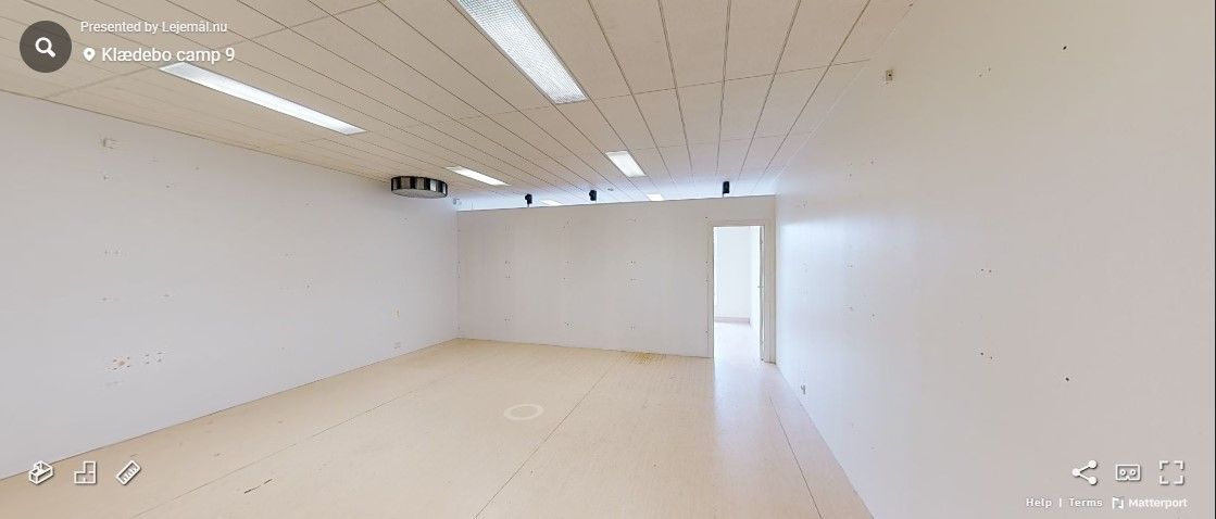 En tom rum med hvide vægge og lysekroner, hvor der er to døre og et kamera på loftet