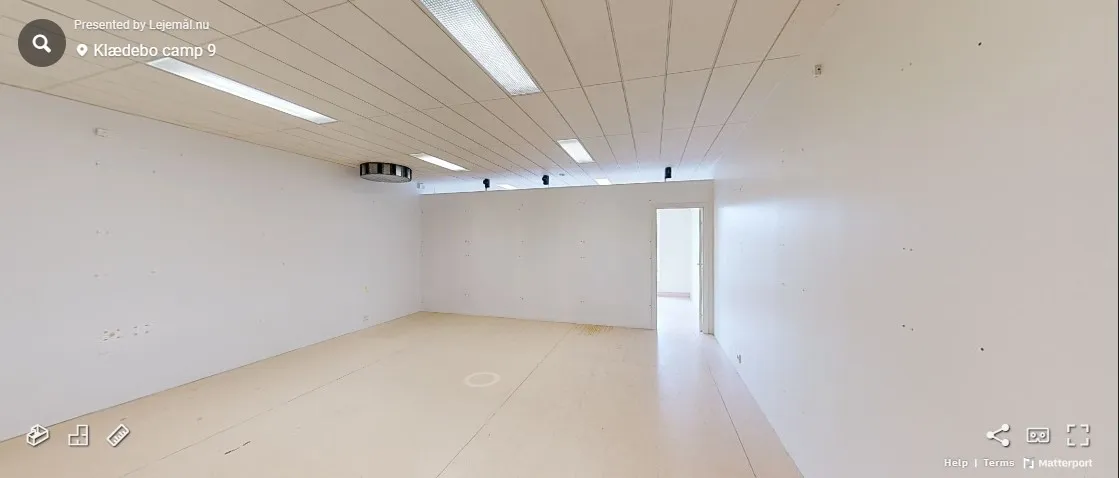 En tom rum med hvide vægge og lysekroner, hvor der er to døre og et kamera på loftet