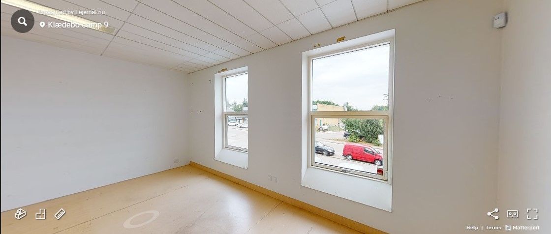 En tom stue med to store vinduer og en snedækket parkeringsplads udenfor med en rød bil og en sort bil i afstand