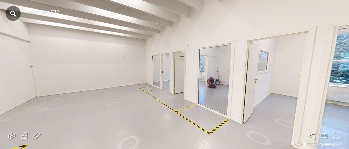 Et tomt lokale med hvide vægge og gulv og flere glasdøre, samt gulvet er markeret med gule og sorte striber