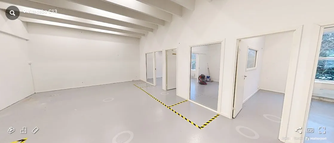 Et tomt lokale med hvide vægge og gulv og flere glasdøre, samt gulvet er markeret med gule og sorte striber