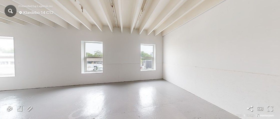 Ledig rum med hvide vægge og lofter, tre vinduer og to lystbøsser i bunden af billedet.